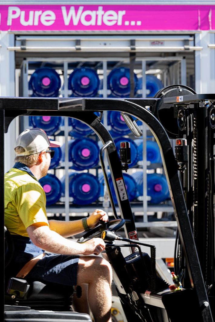 Worker Sitting on a Forklift in Front of Stacked Blue Water Jugs Labeled “pure Water” — So Fresh Wide Bay in Thabeban, QLD