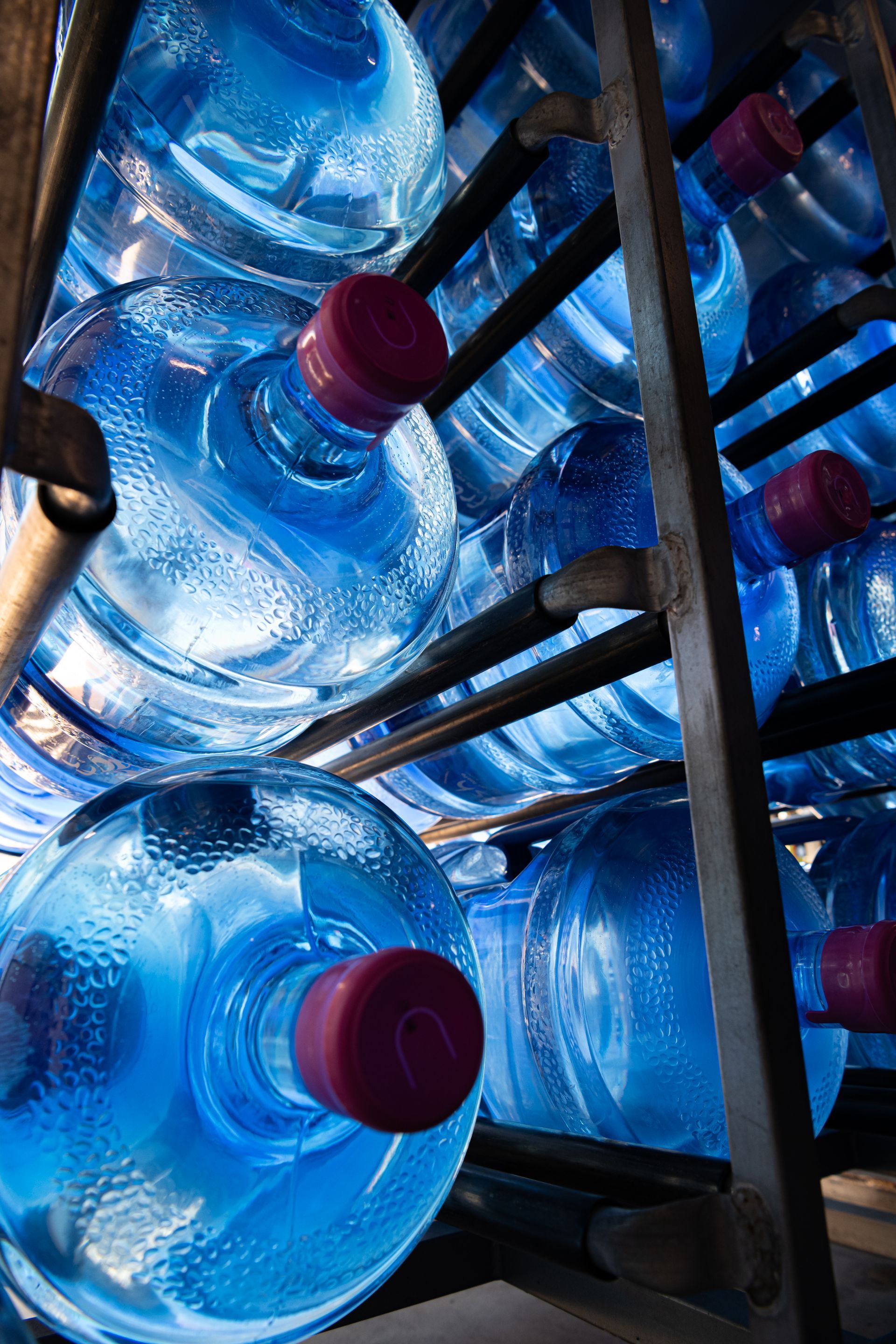 Large water bottles with blue-tinted plastic and pink caps stacked on metal racks — So Fresh Wide Bay in Bargara, QLD