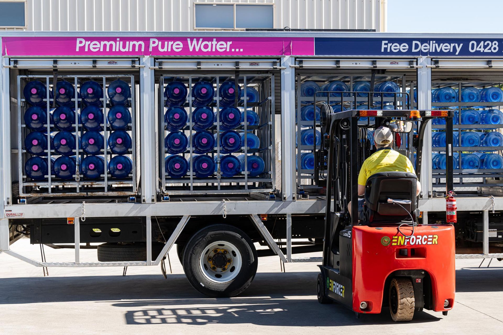 Worker drives forklift beside bottled water delivery truck on a city street