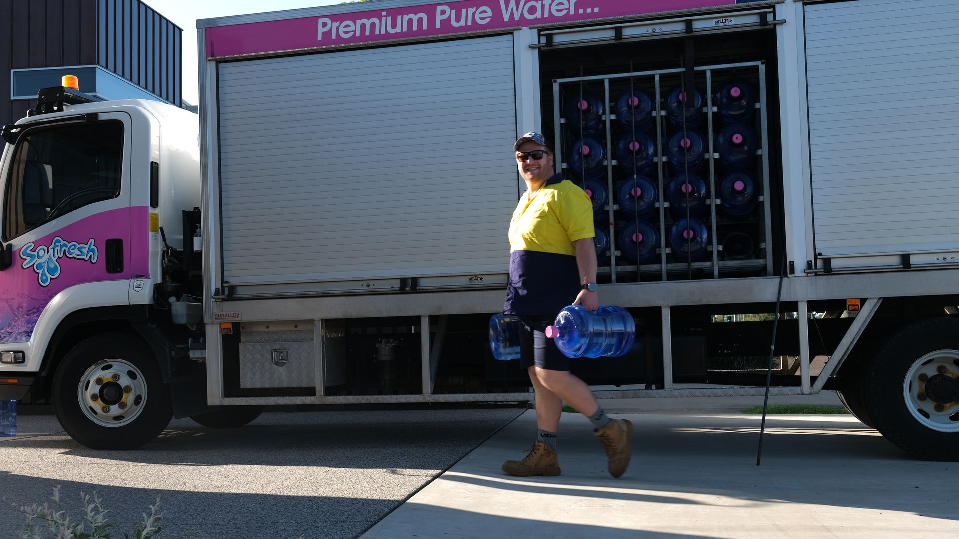 Delivery truck with open side, a worker carrying a blue water container, and stacked bottles inside.