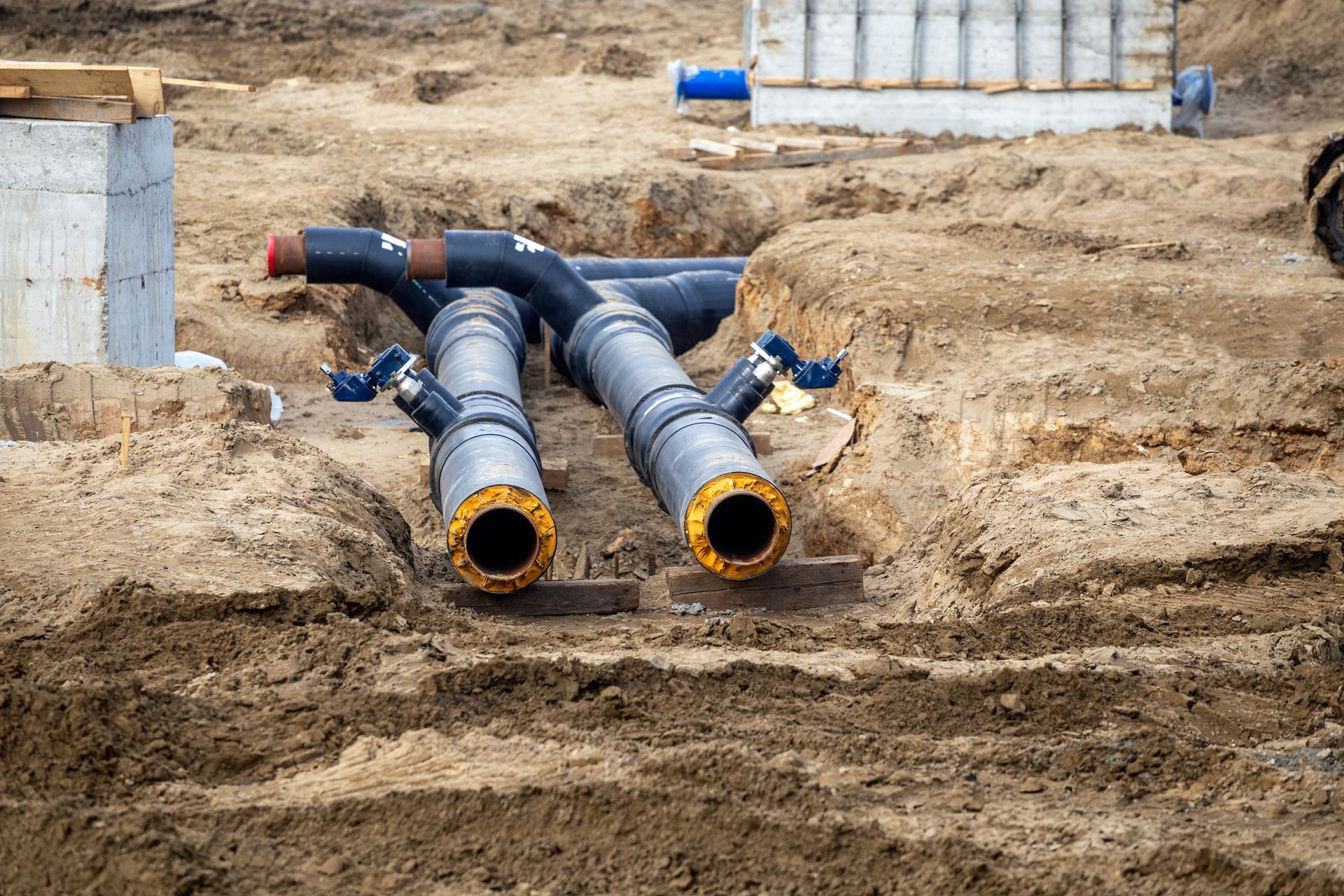 Two large black pipes with yellow ends in a dirt trench, likely for infrastructure.