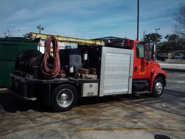 Red work truck with a roll-up side compartment, parked in a lot, with ladder on top.