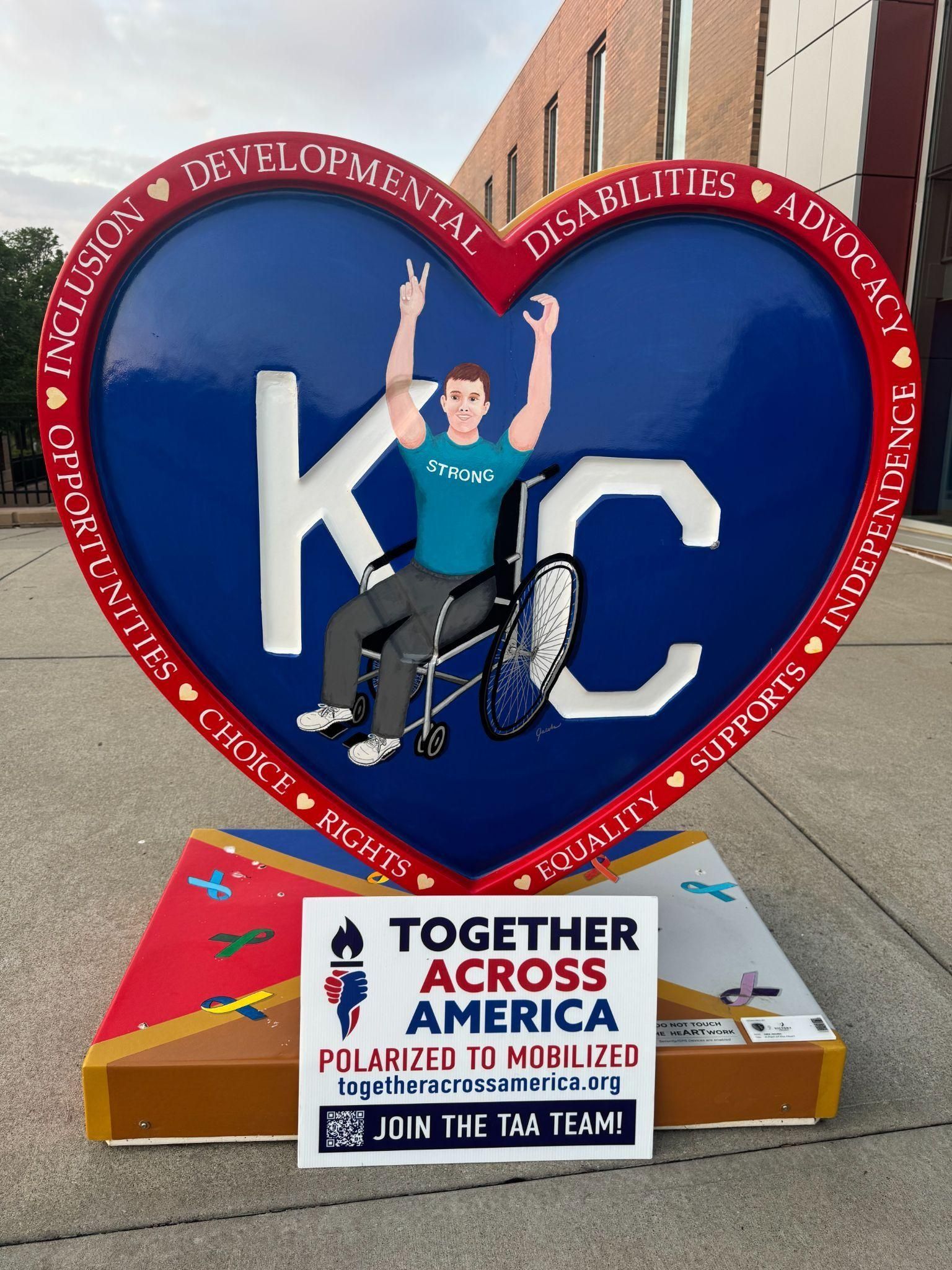 A heart-shaped KC sculpture features a person in a wheelchair, with 