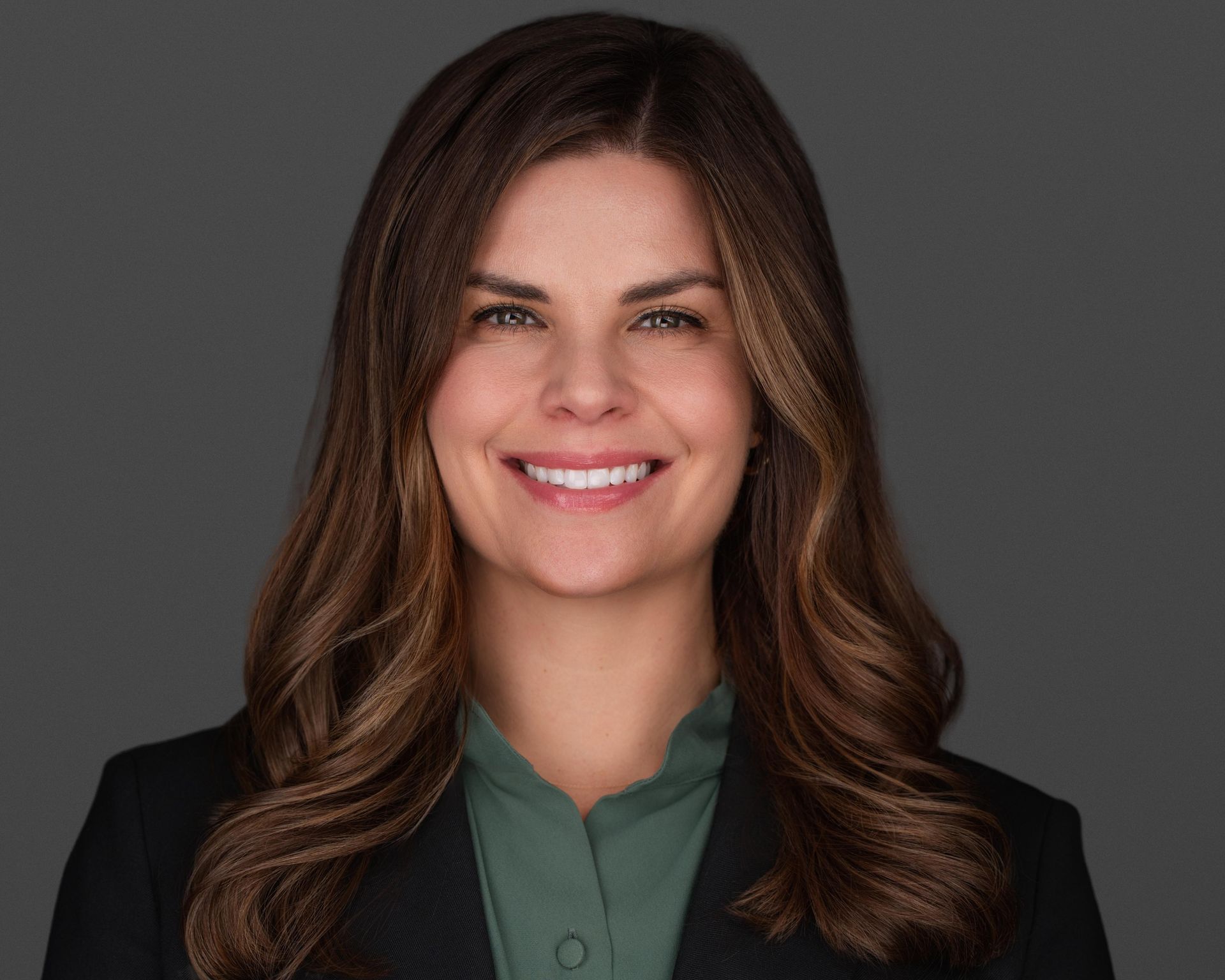 A woman in a blue shirt and black jacket is smiling for the camera.