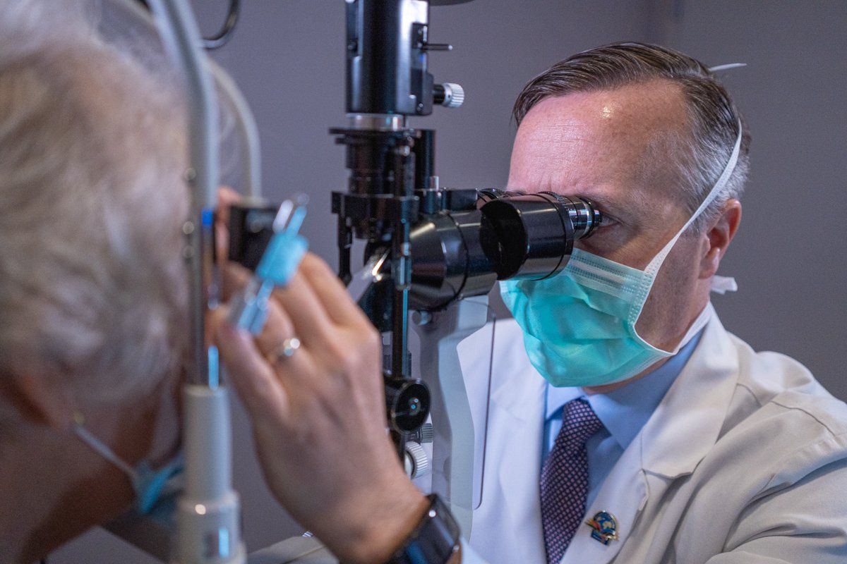 A doctor wearing a mask is examining a patient 's eye with a microscope.