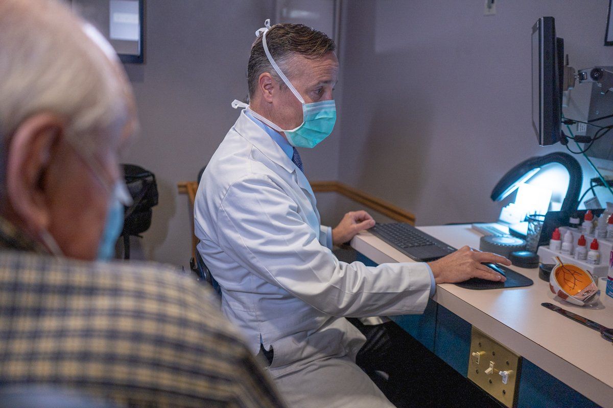 A man wearing a mask is sitting at a desk using a computer.
