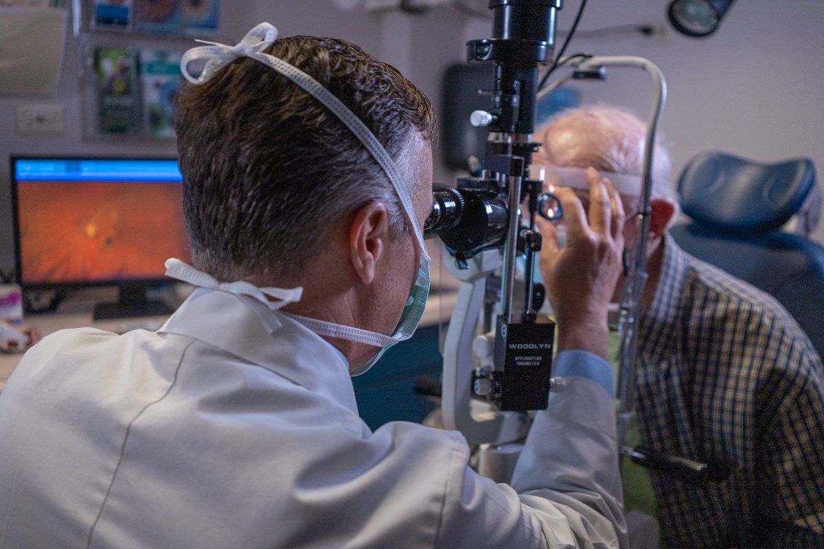 A doctor is examining an older man 's eye with a microscope.