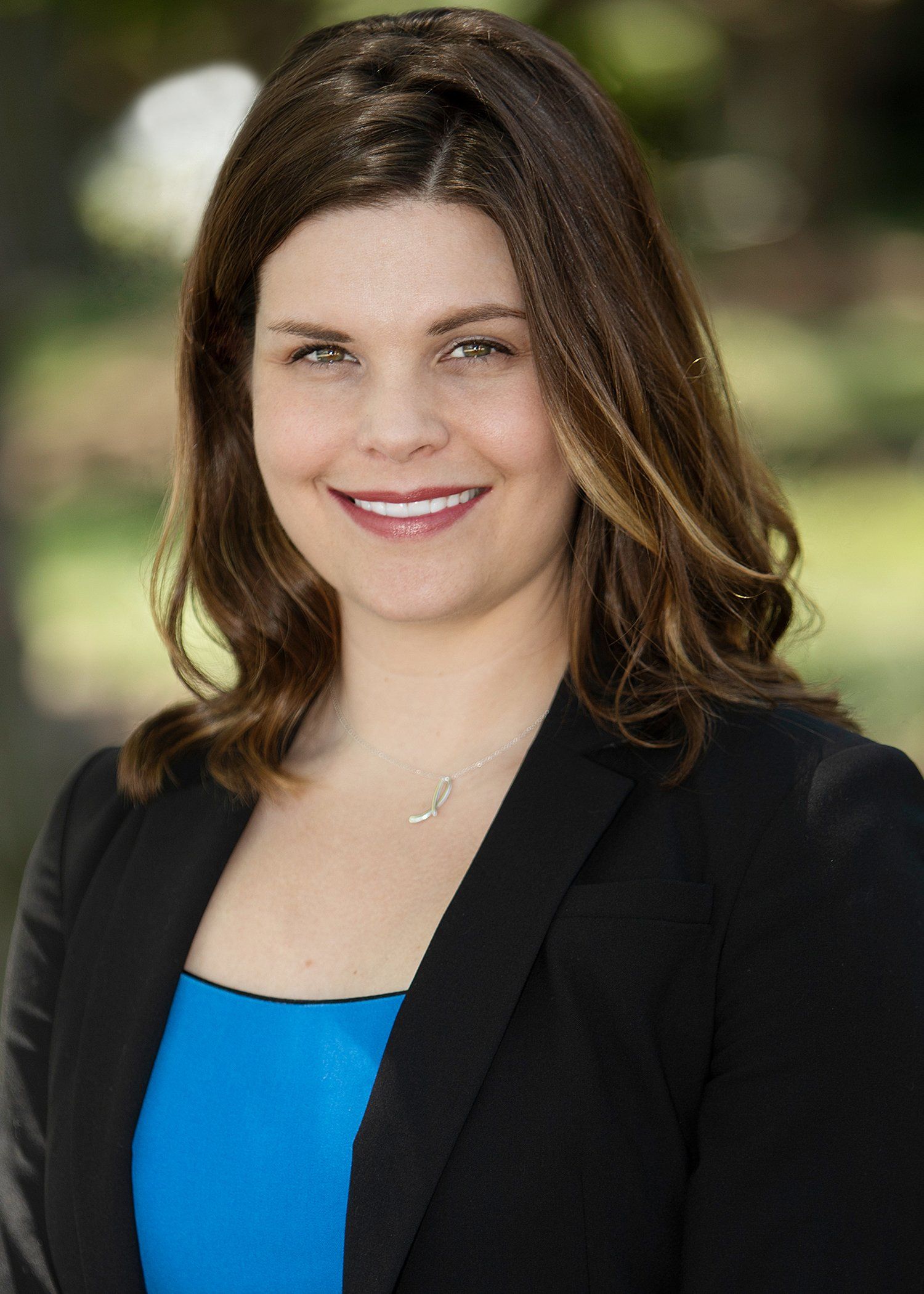 A woman in a blue shirt and black jacket is smiling for the camera.