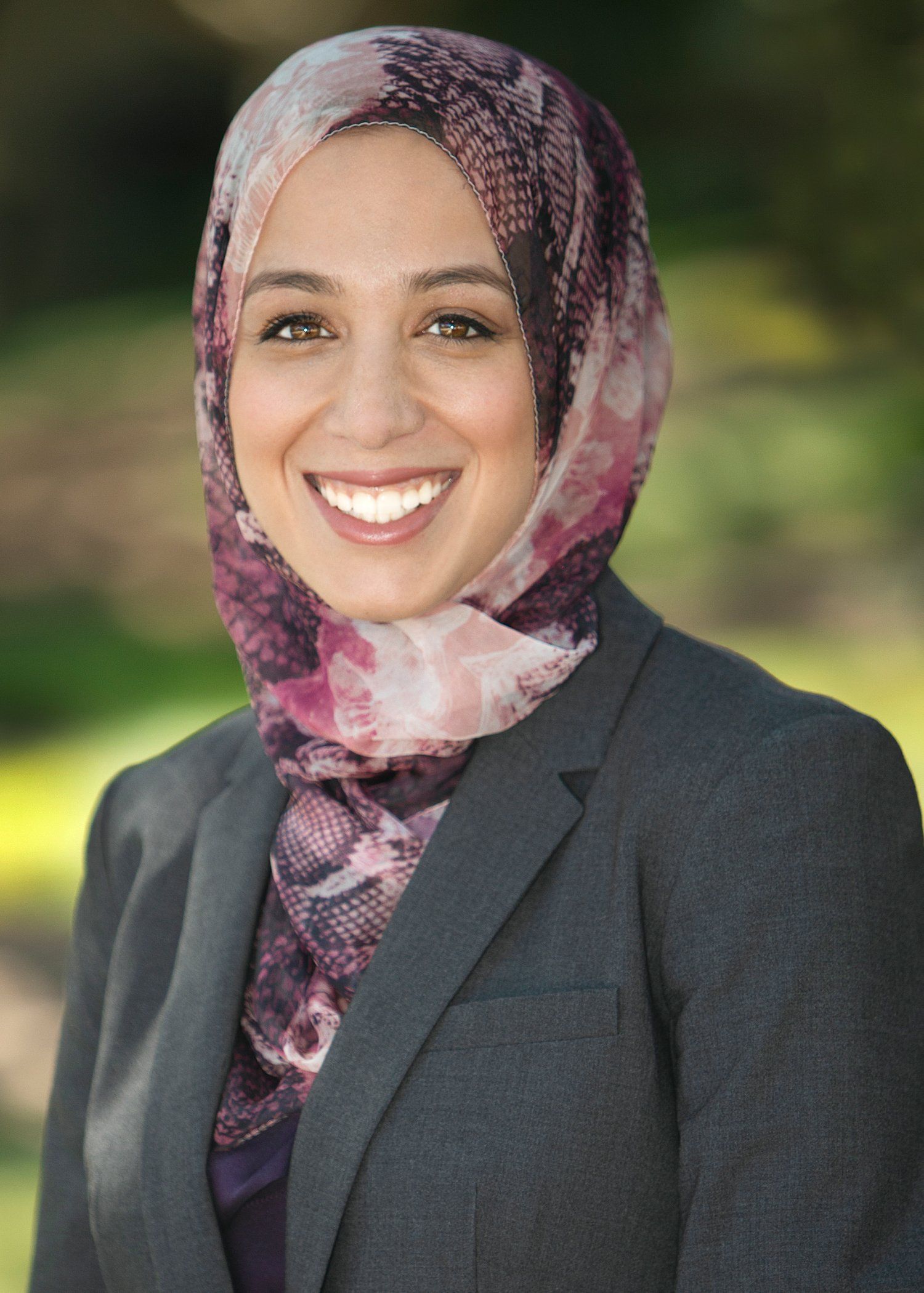 A woman wearing a hijab and a suit is smiling for the camera