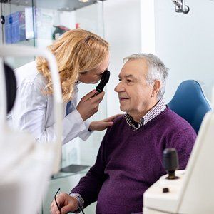 A woman is examining an older man 's eye with a magnifying glass.