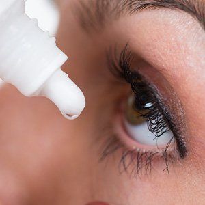 A woman is applying eye drops to her eye.