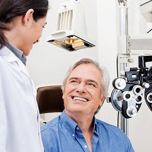 A man is smiling while having his eyes examined by an ophthalmologist.