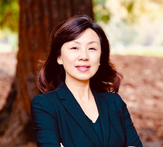 A woman in a suit is standing in front of a tree with her arms crossed.