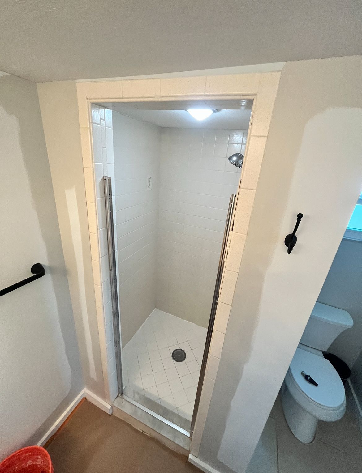 Shower with glass door in a bathroom, white tile and walls. Toilet visible.