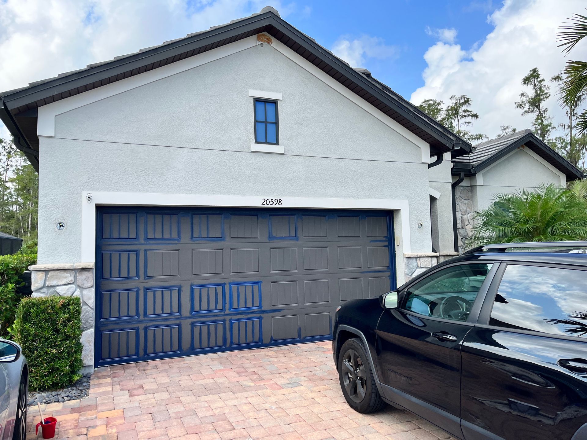 Garage door of a house with a black SUV parked in front. Blue accents on the garage door, light blue exterior.