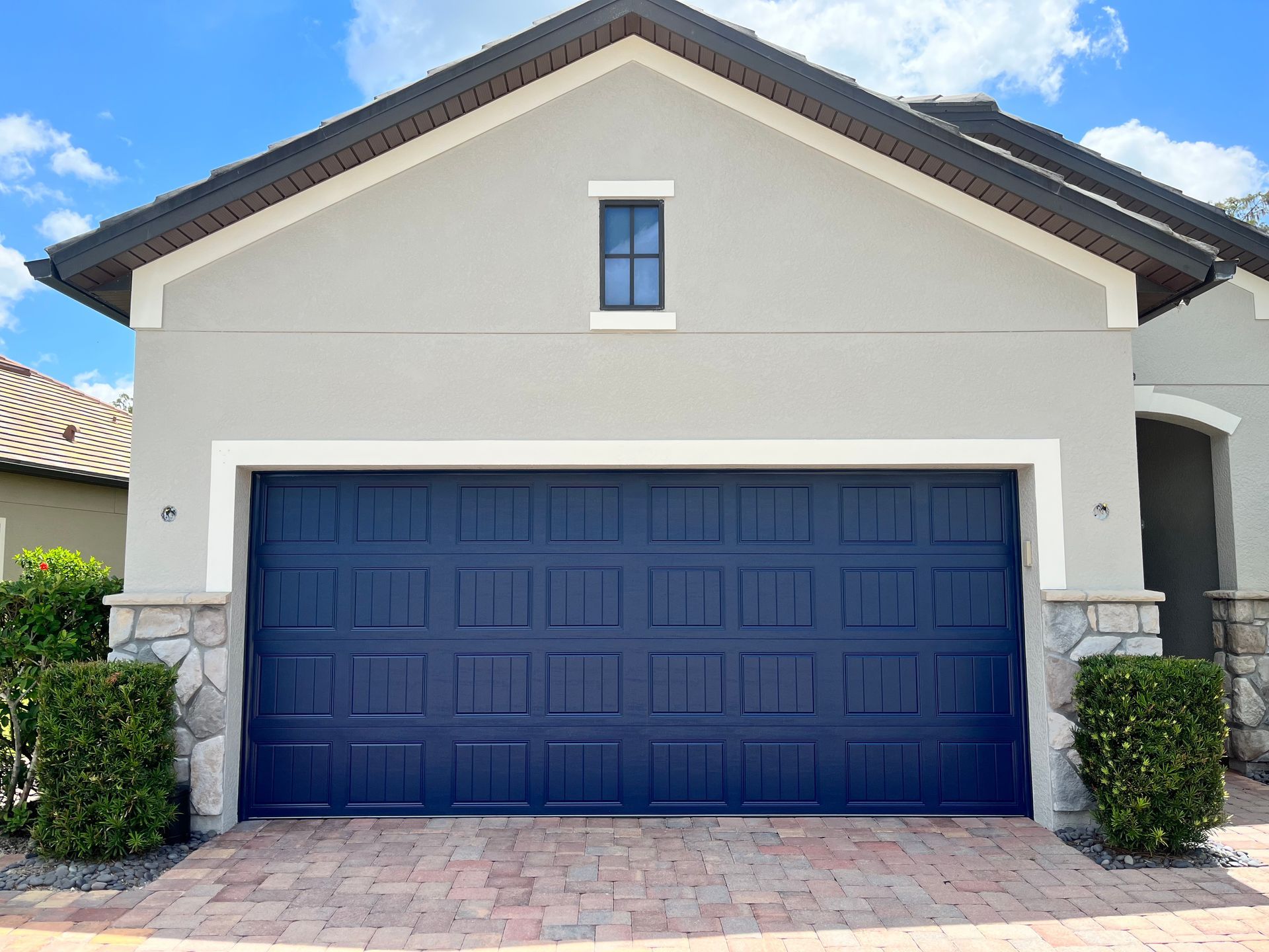 Blue garage door on a gray stucco house with stone accents and a small window.