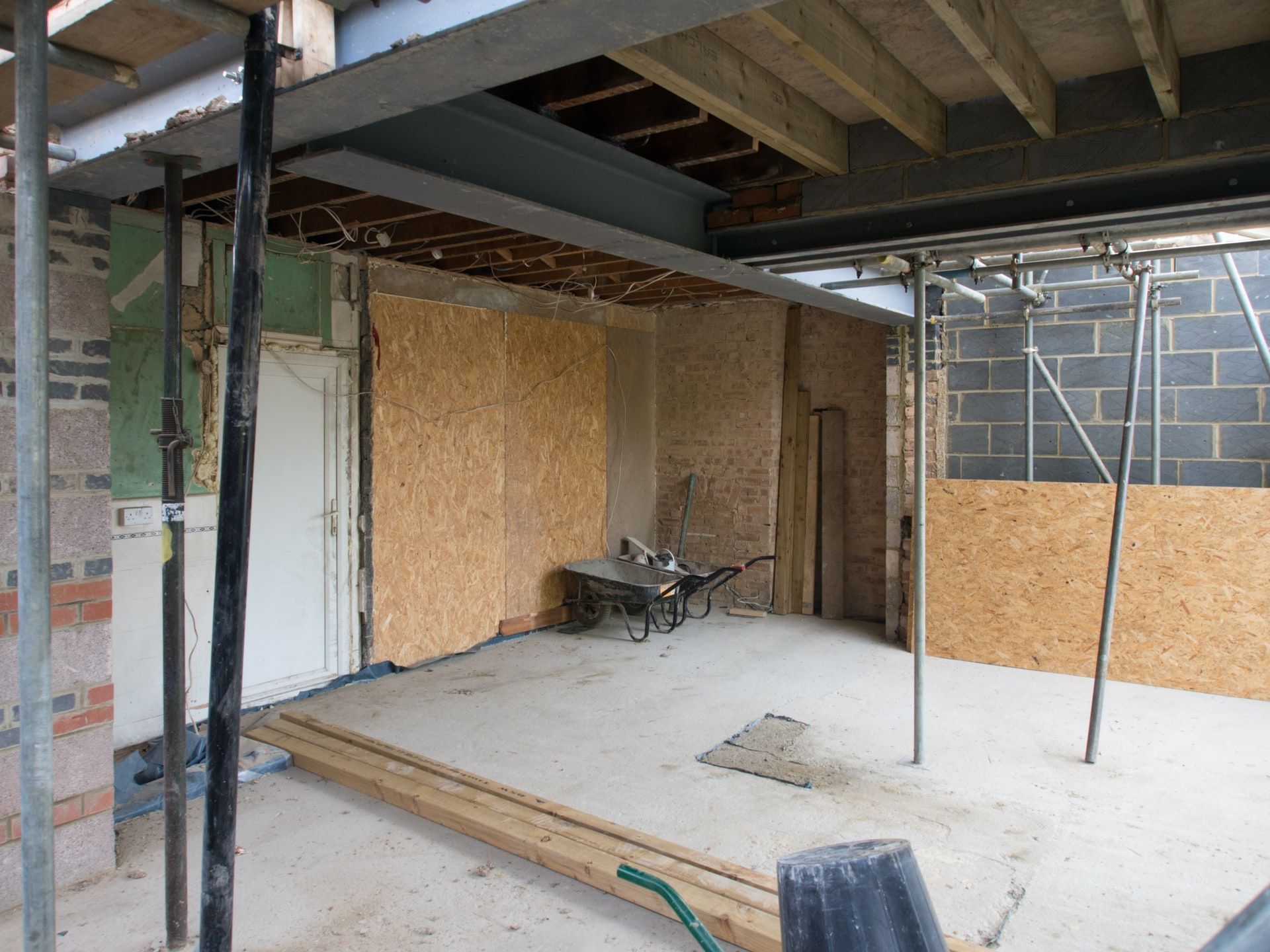 Construction site interior: room with exposed walls, steel beams, scaffolding, and a wheelbarrow.