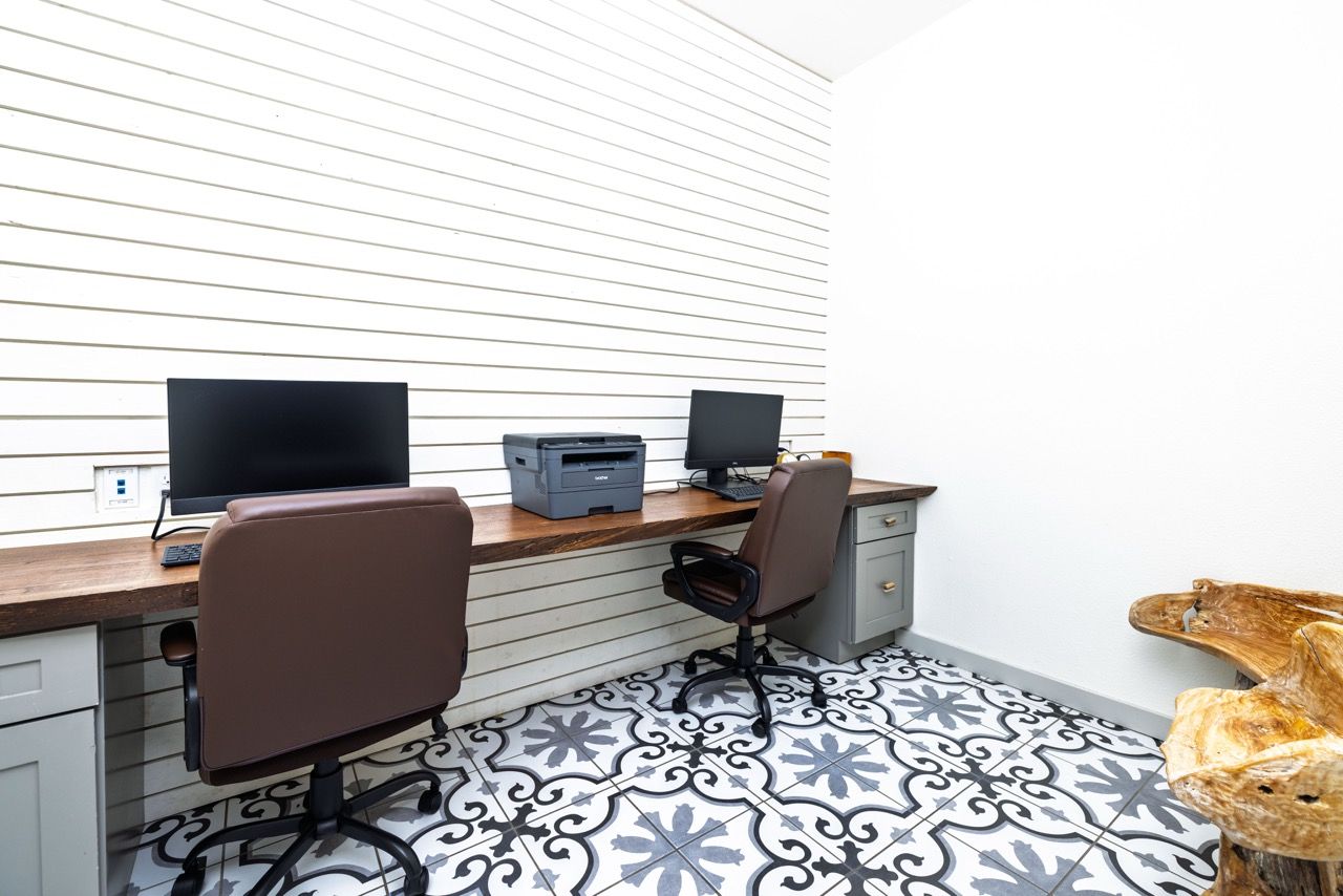 Two computer desks with chairs and a printer in a communal office area.