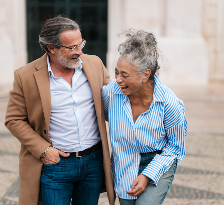 Man with coat and woman walking, laughing, arm in arm. Paved setting.