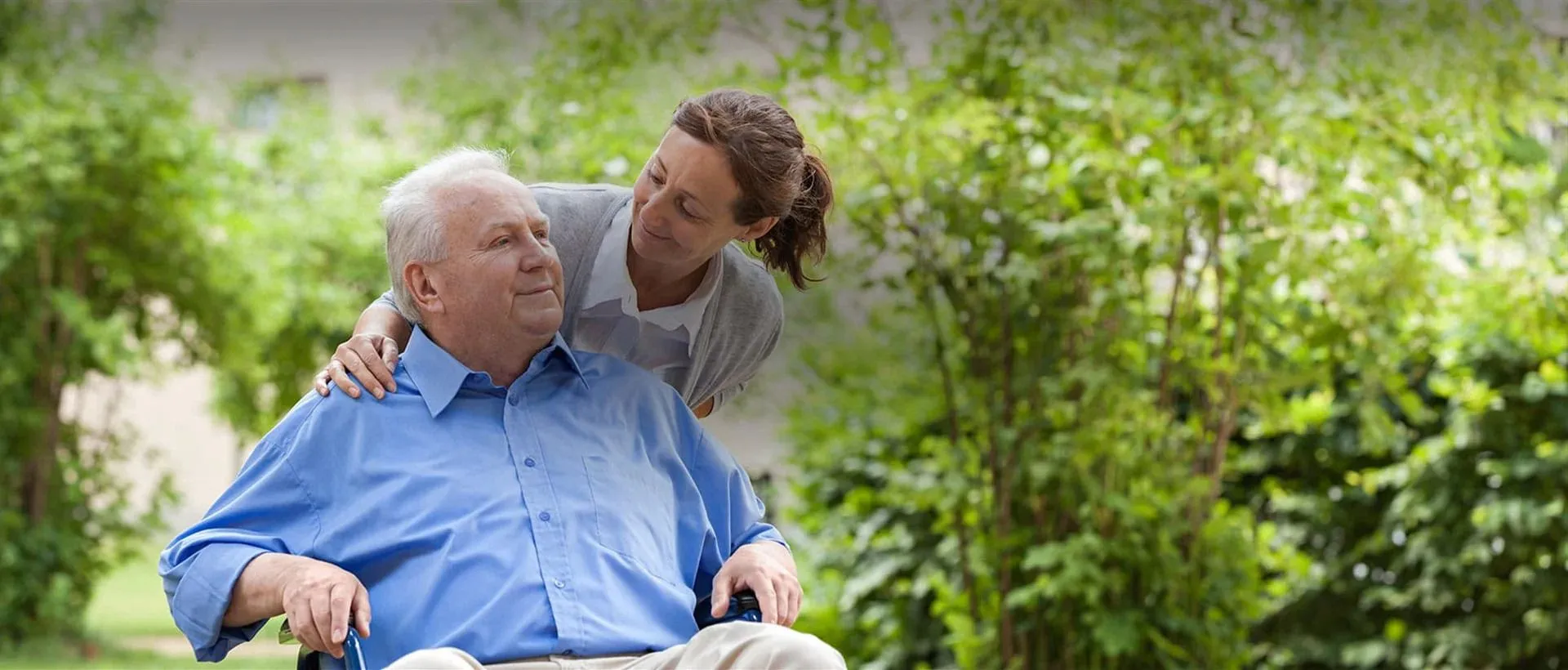 A woman is standing next to an older man in a wheelchair.