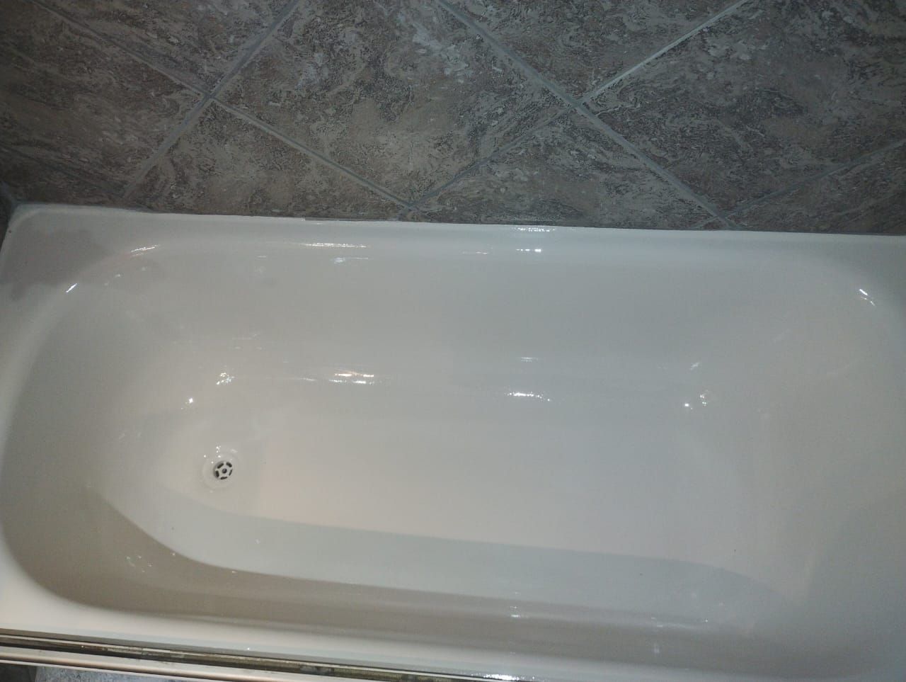 Bañera blanca con desagüe, situada contra una pared de azulejos grises.