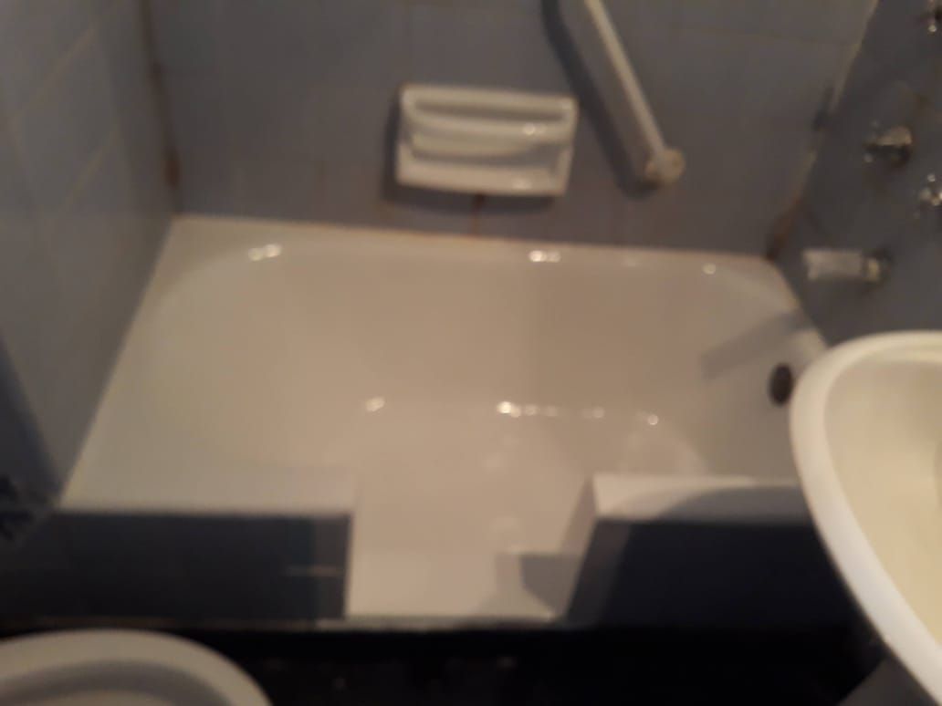Bañera blanca con escalón incorporado, jabonera y barra de apoyo, en un baño alicatado.