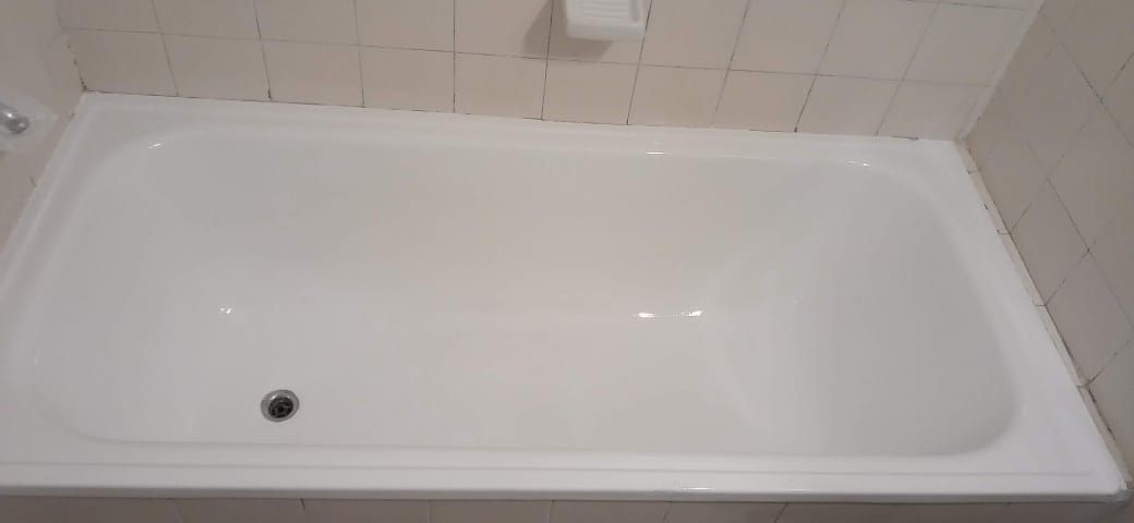 Una bañera blanca en un baño, con desagüe visible. Azulejos en la pared superior.