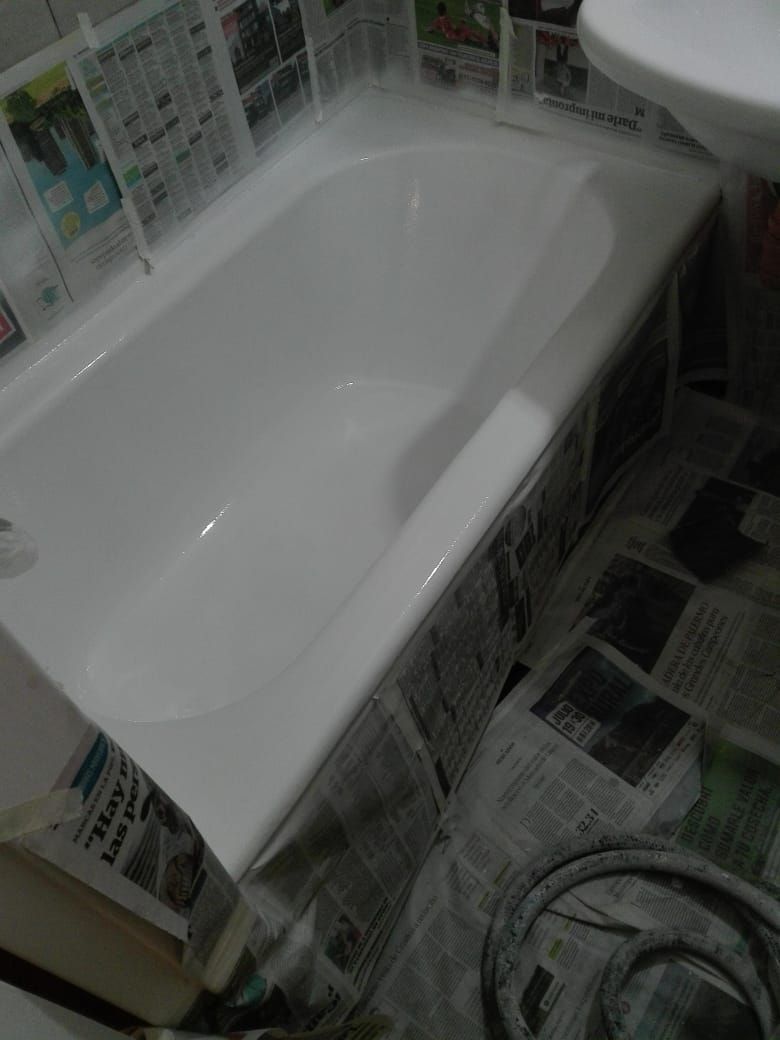 Una bañera blanca recién pintada en un baño, con papel de periódico cubriendo el piso circundante.