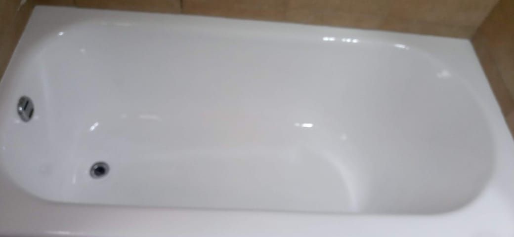 Una bañera blanca con desagüe y grifo, sobre un fondo de azulejos.