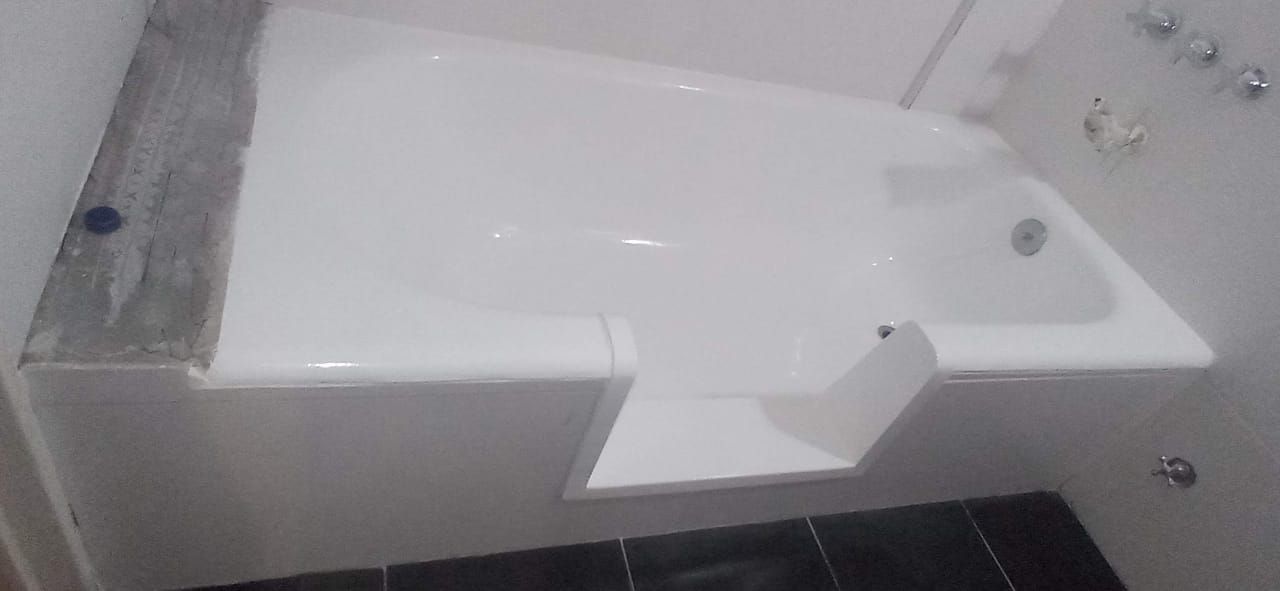 Bañera blanca con diseño de acceso a nivel, suelo de baldosas negras y herrajes metálicos en un baño.