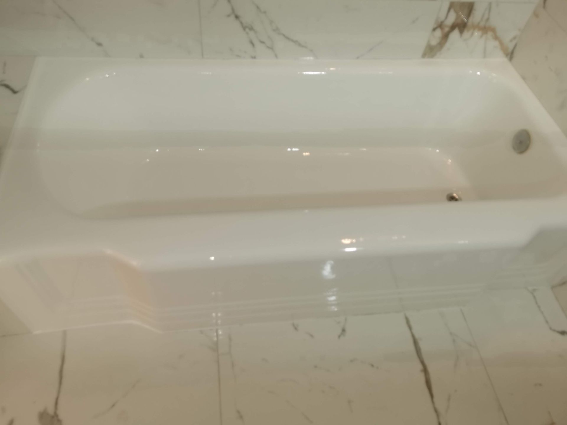 Bañera rectangular blanca sobre suelo de baldosas de mármol blanco y gris.