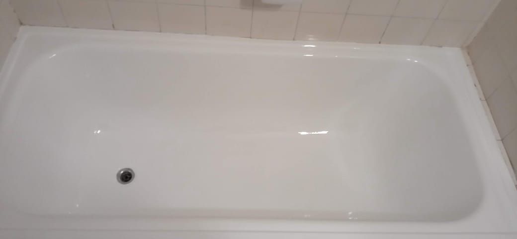 Una bañera blanca y limpia. El desagüe es visible en el fondo. La bañera está rodeada de azulejos blancos.