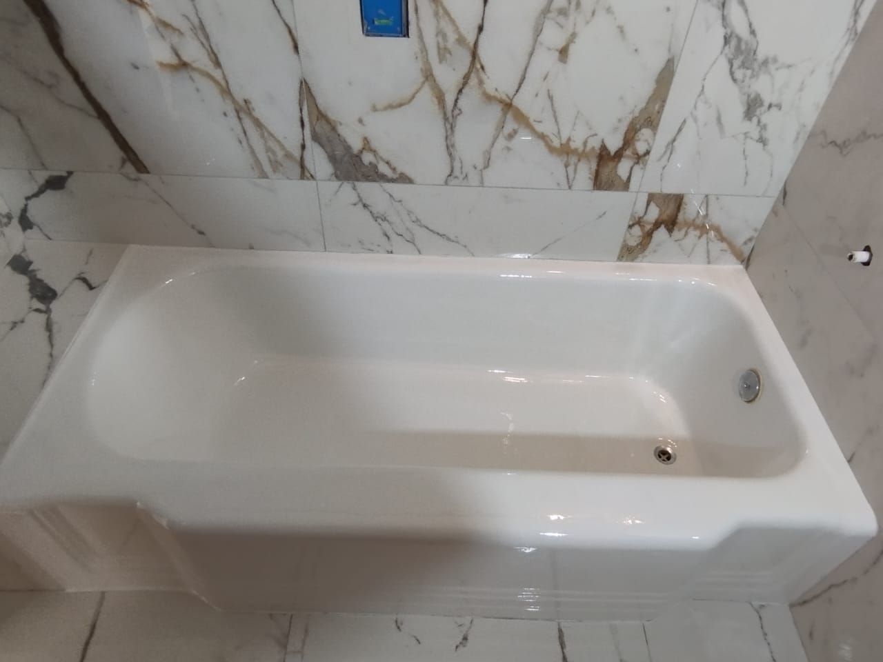 Bañera blanca instalada, sobre baldosas con diseño de mármol, con grifo.