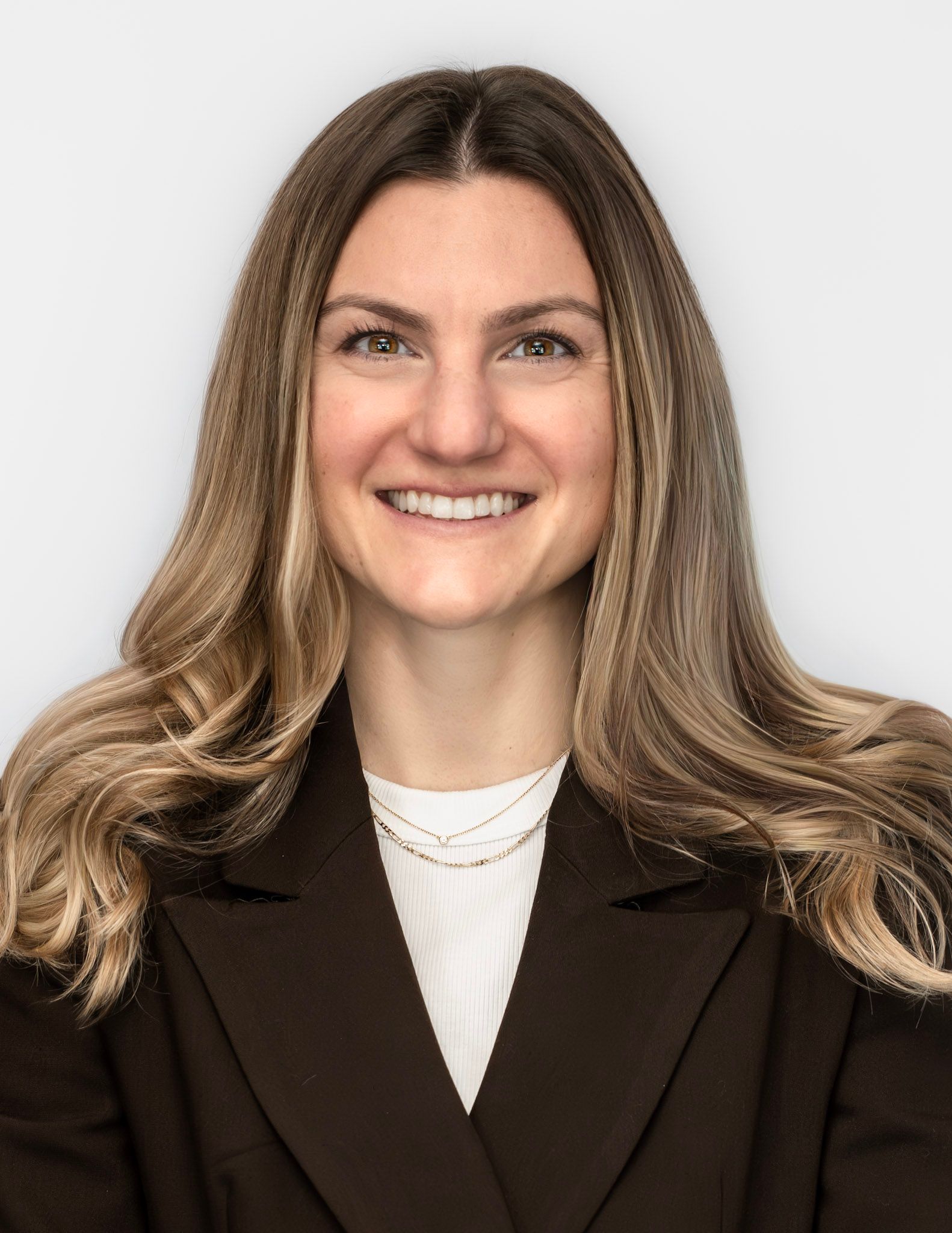 Woman smiling, wearing a dark blazer and a white shirt. Light hair. White background.