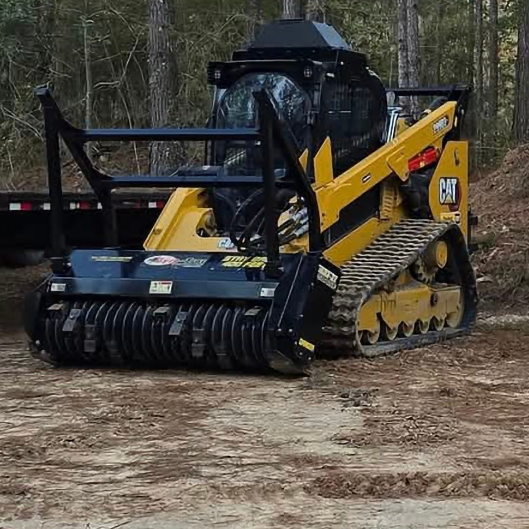 Yellow Caterpillar skid steer with mulcher attachment in a wooded area.