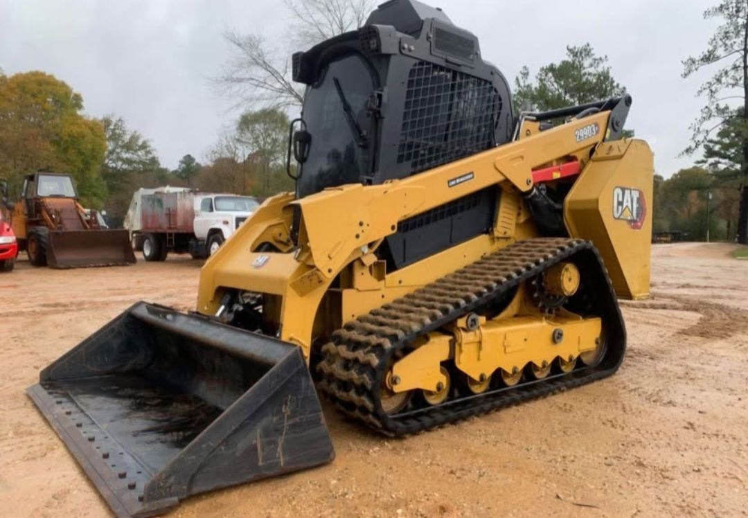 Yellow Caterpillar track loader with bucket outdoors on a cloudy day.