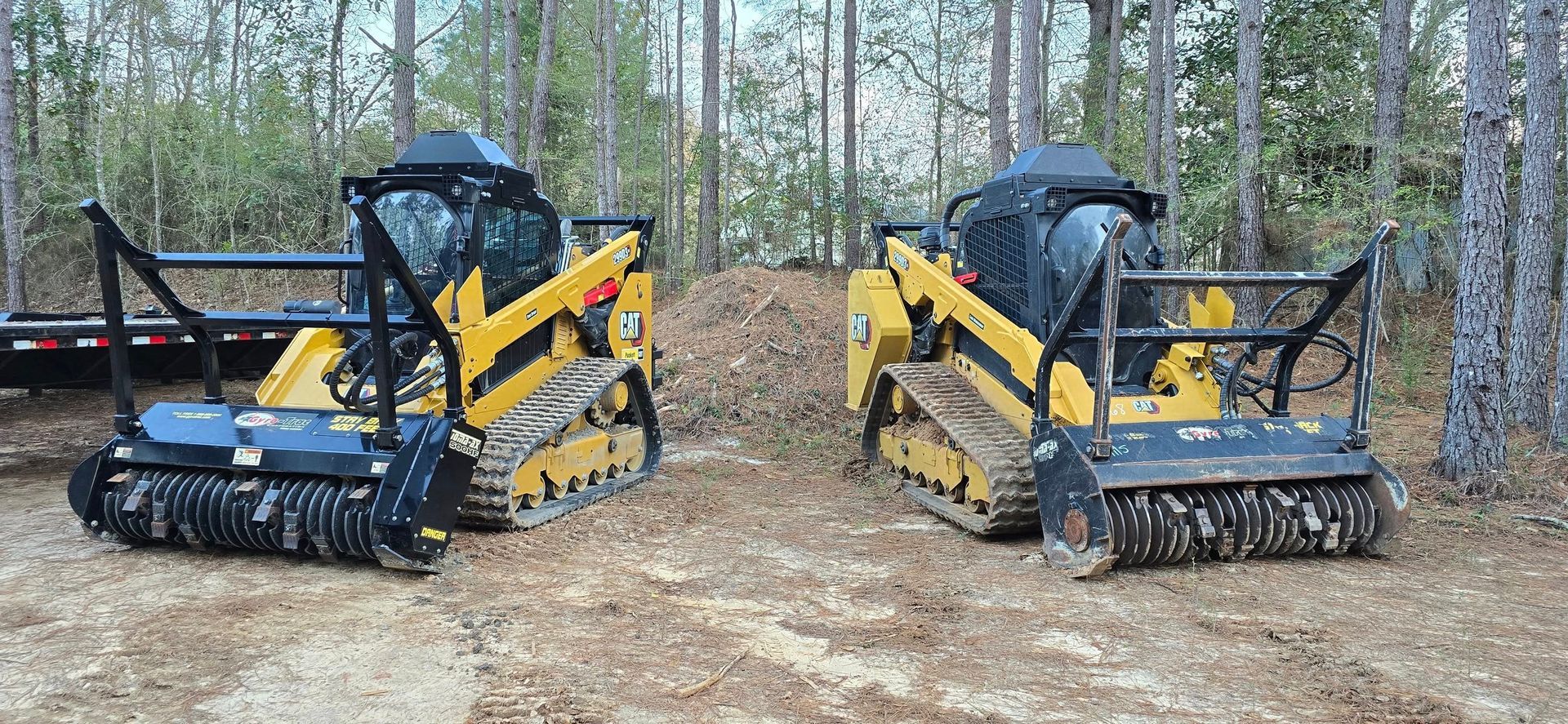 Two yellow tracked mulchers in a wooded area.