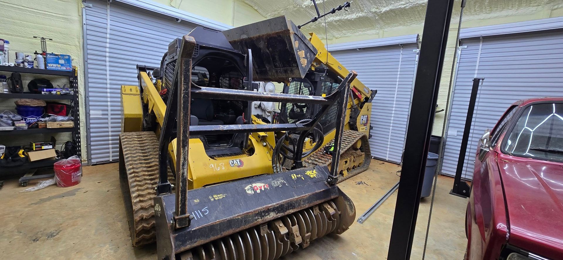 Yellow skid steer with a brush cutter attachment in a garage.
