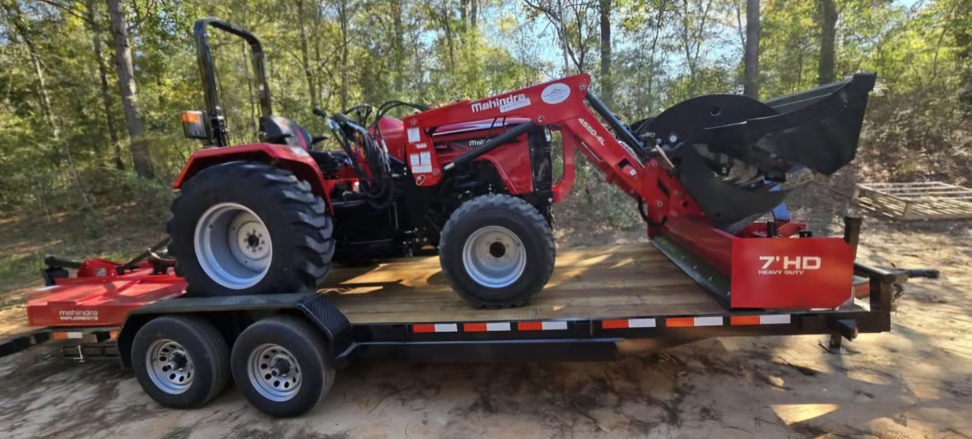 Red tractor with a bucket on a trailer in a wooded area.