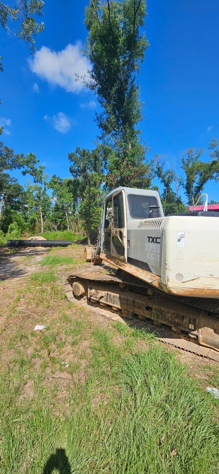 A white bulldozer with tracks sits on grass beside a log. Blue sky and trees in background.