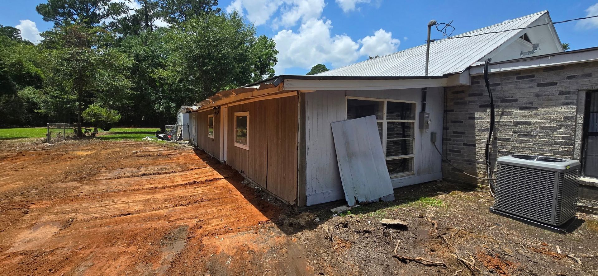 A house under renovation with wood siding and a bare yard, on a sunny day.