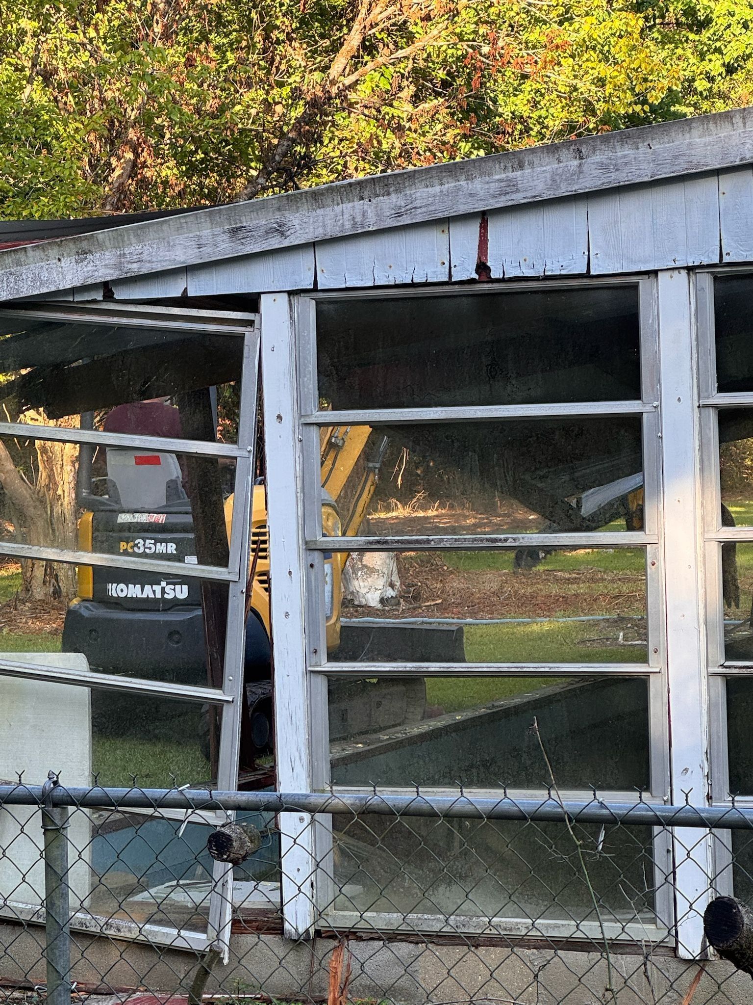 White-framed windowed structure with a Komatsu excavator visible through the glass.