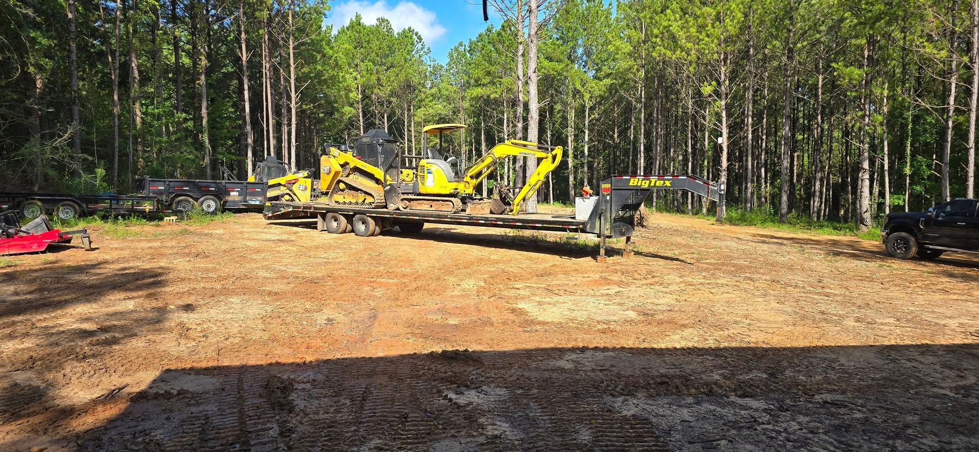 Yellow excavators on trailers in a clearing, surrounded by trees.
