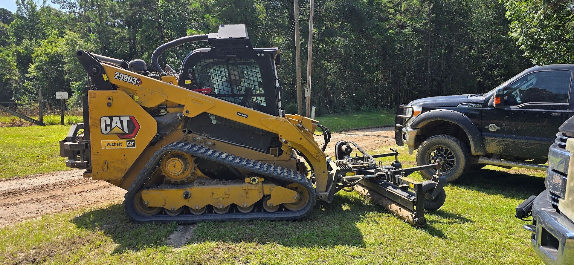 Yellow CAT skid steer with an attached implement next to a black pickup truck on a grassy area.