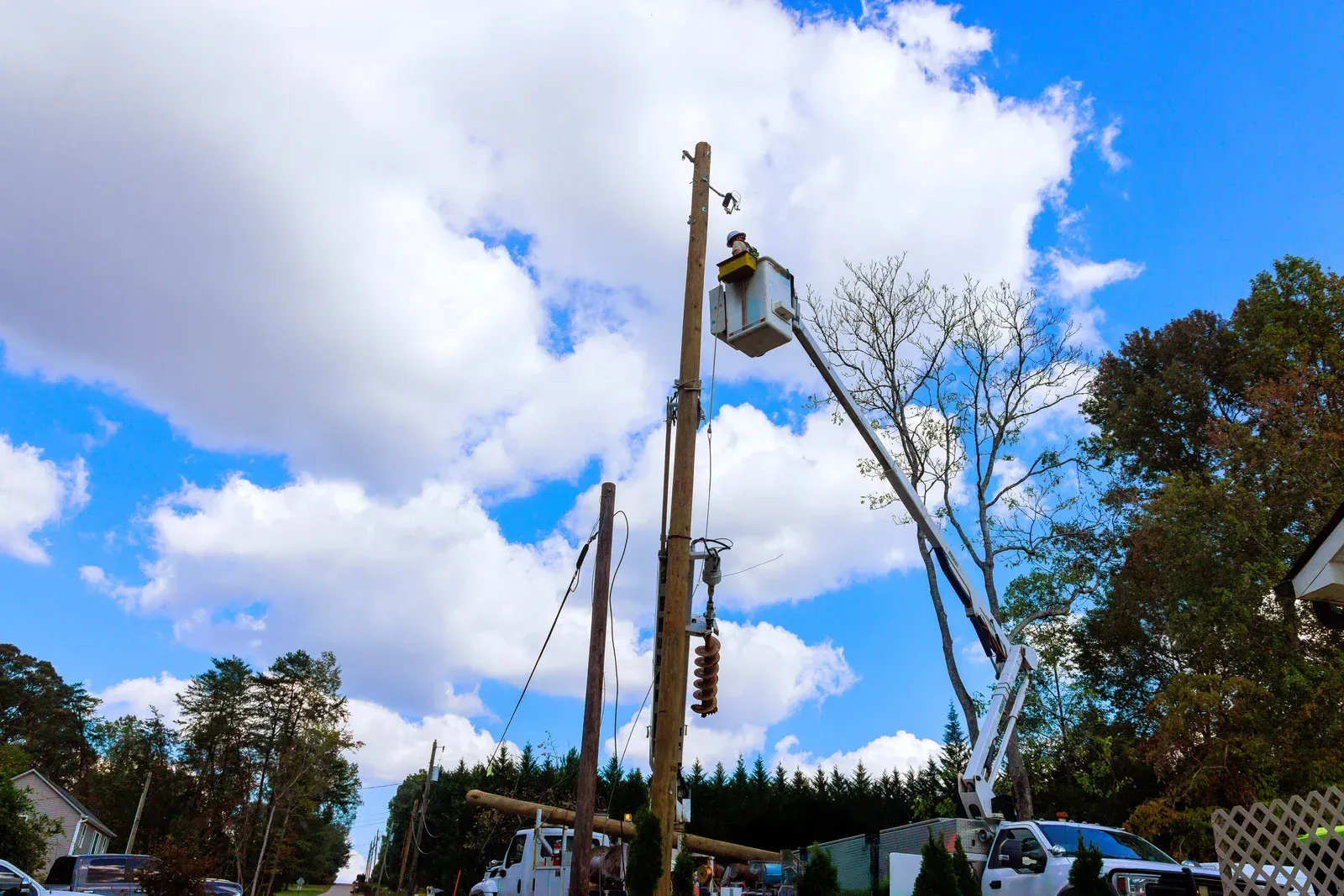 Black truck hauling a trailer with construction equipment on a gravel road, surrounded by trees.