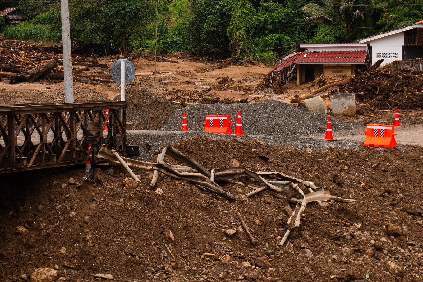 Road blocked by mud and debris after a landslide, orange traffic cones in foreground.