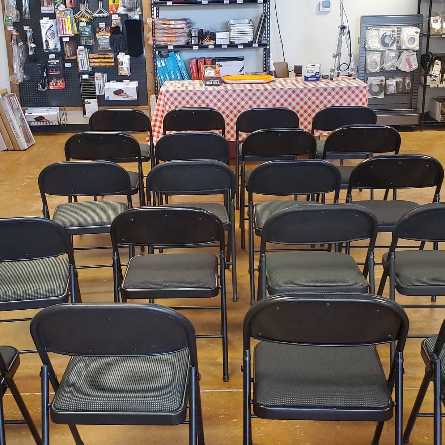 Rows of folding chairs in a room with a table in the background