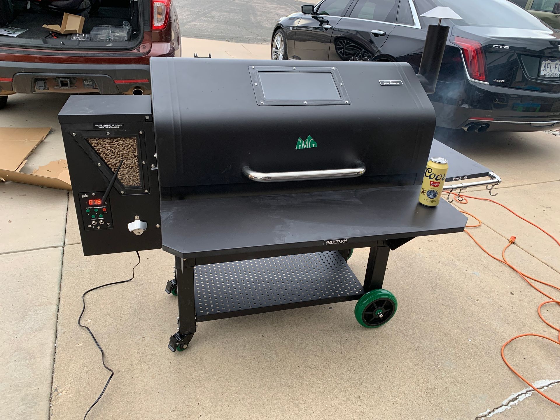 A black grill is sitting in a driveway next to a car.