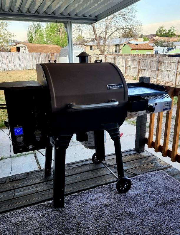 A grill is sitting on a wooden deck under a covered porch.