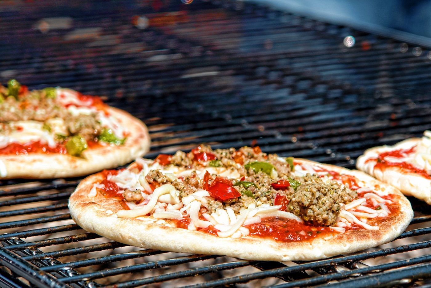 Three pizzas are cooking on a grill.